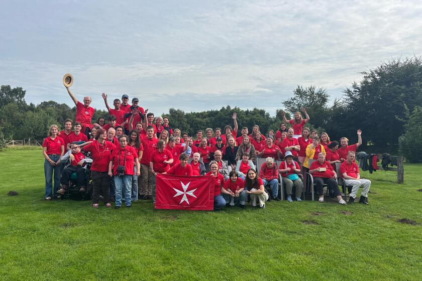 Gruppenbild der Integra-Freizeit 2025: Gäste und Betreuende in roten Shirts auf einer Wiese, mit Johanniterfahne