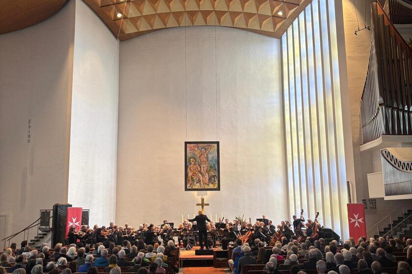 Orchester und volles Publikum beim Benefizkonzert der Johanniter in einer Kirche, seitlich die Johanniterfahnen