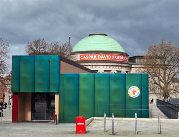 Grün-blauer Neubau der Bahnhofsmission am Hamburger Hauptbahnhof, dahinter die Kuppel der Kunsthalle