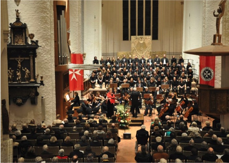 Benefizkonzert der Johanniter-Hilfsgemeinschaft: Orchester und Chor in einer Kirche vor vollen Bänken
