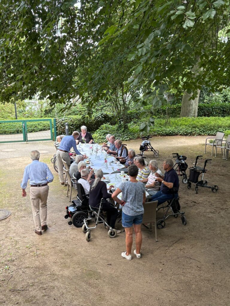 Lange Kaffeetafel im Garten der Auguste-Viktoria-Stiftung, Gäste und Helfende an den Tischen