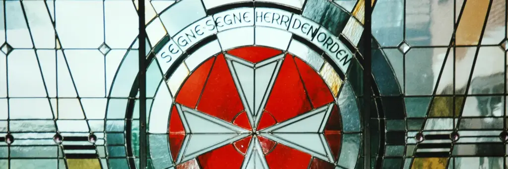 Kirchenfenster mit dem Johanniterkreuz und der Umschrift „Segne segne Herr den Orden“
